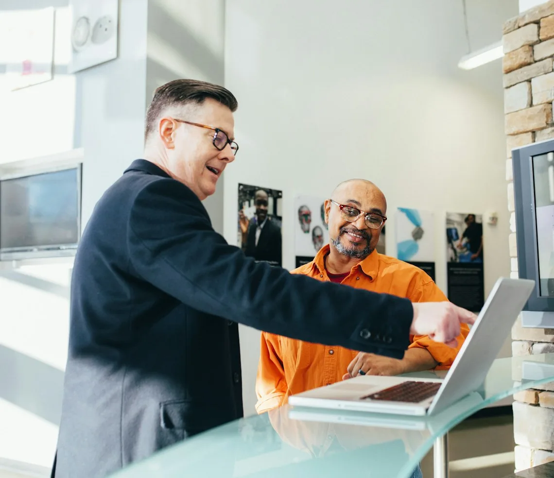 An insurance agent greeting a client across a desk with a laptop
