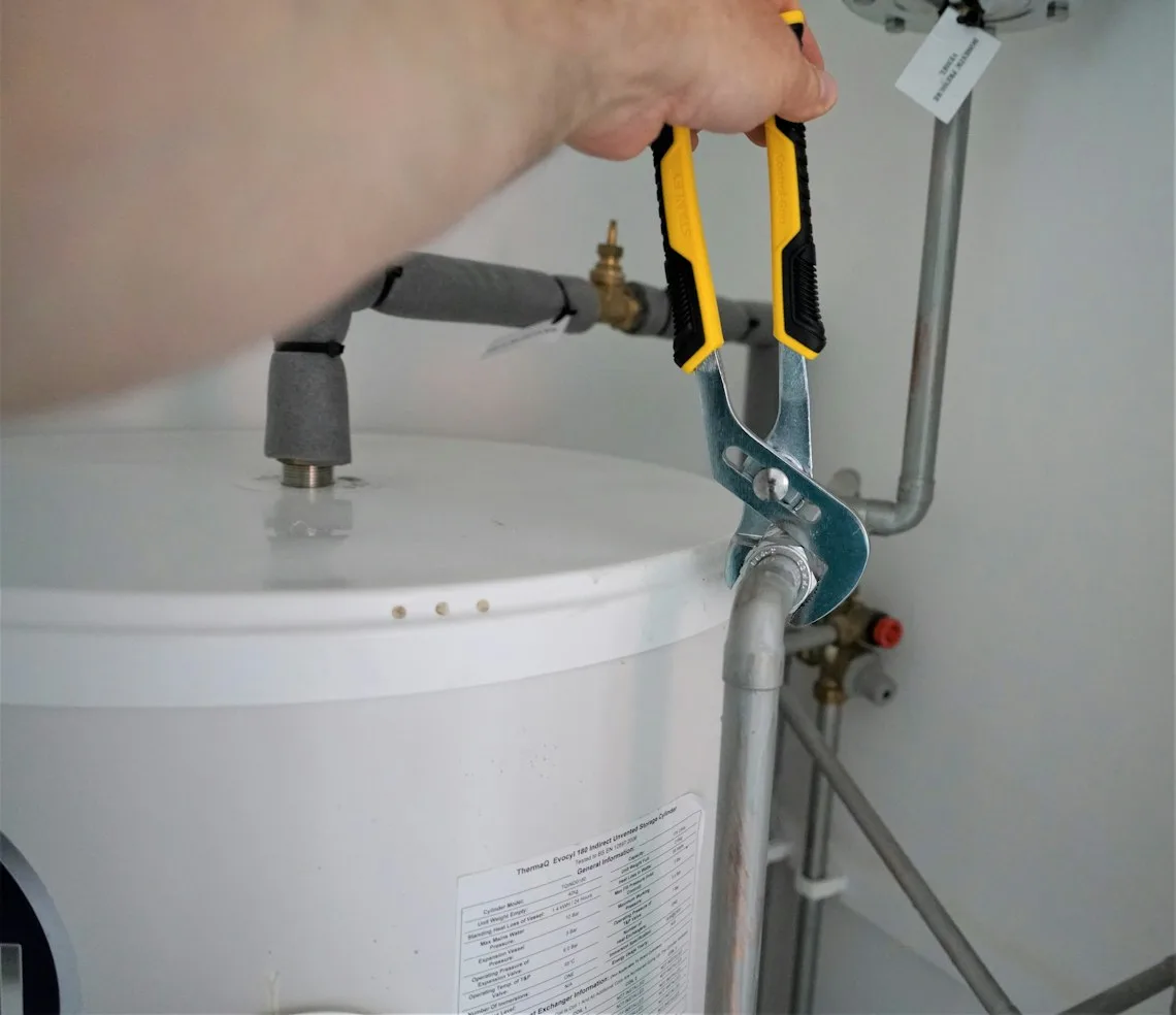 A plumber tightening a joint on the pipework of a water heater