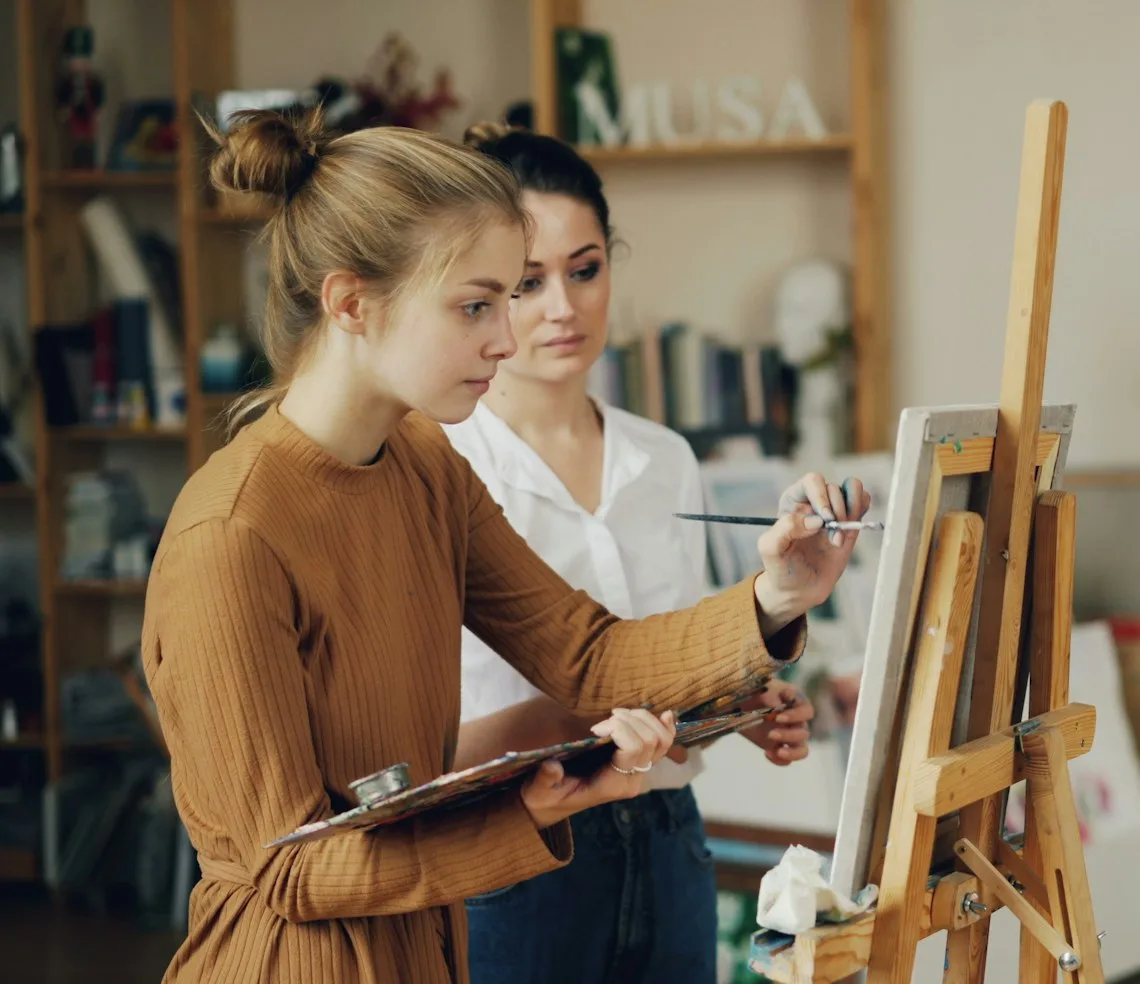 A teacher helping a student at the easel in an art studio