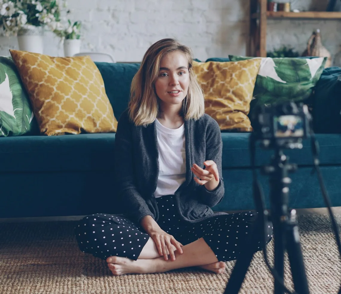 A blogger recording a video on a tripod-mounted camera in the living room