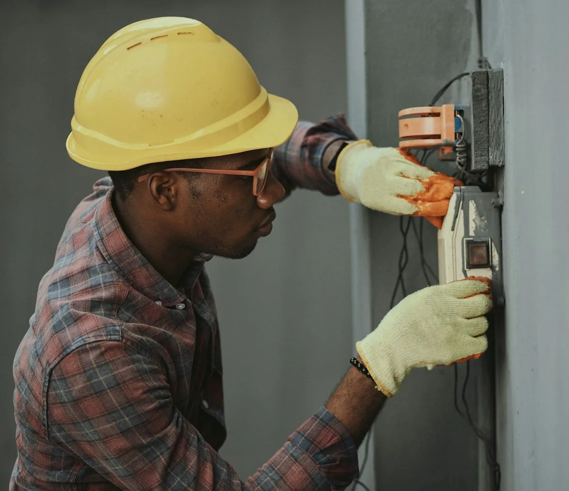 An electrician in a hard hat testing a wall-mounted consumer unit