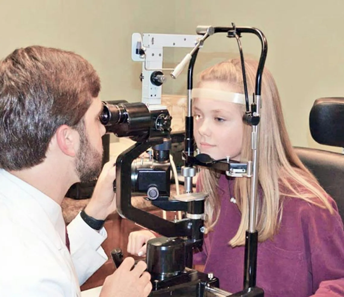 An optometrist testing a girl’s eyesight at the slit lamp