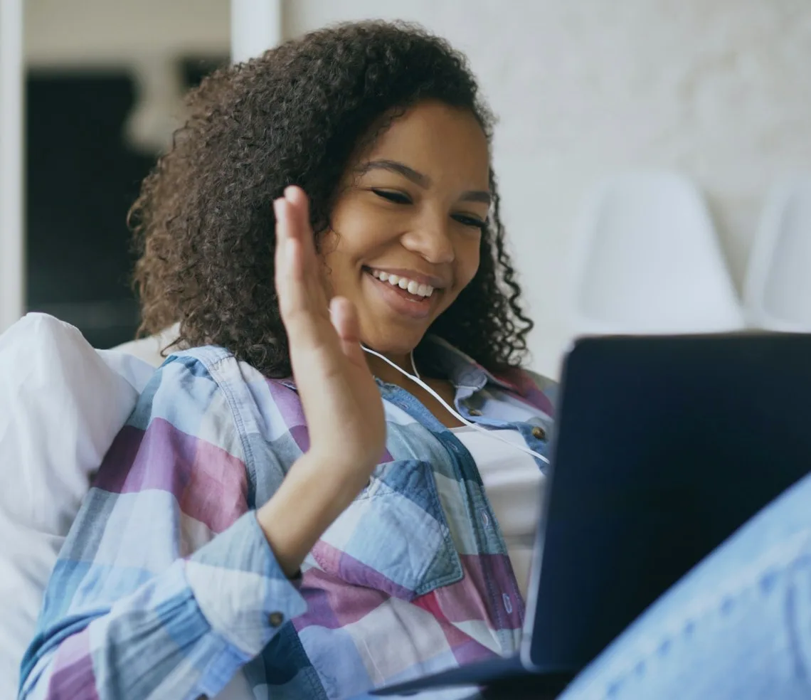 A student waving at the start of an online lesson on a laptop