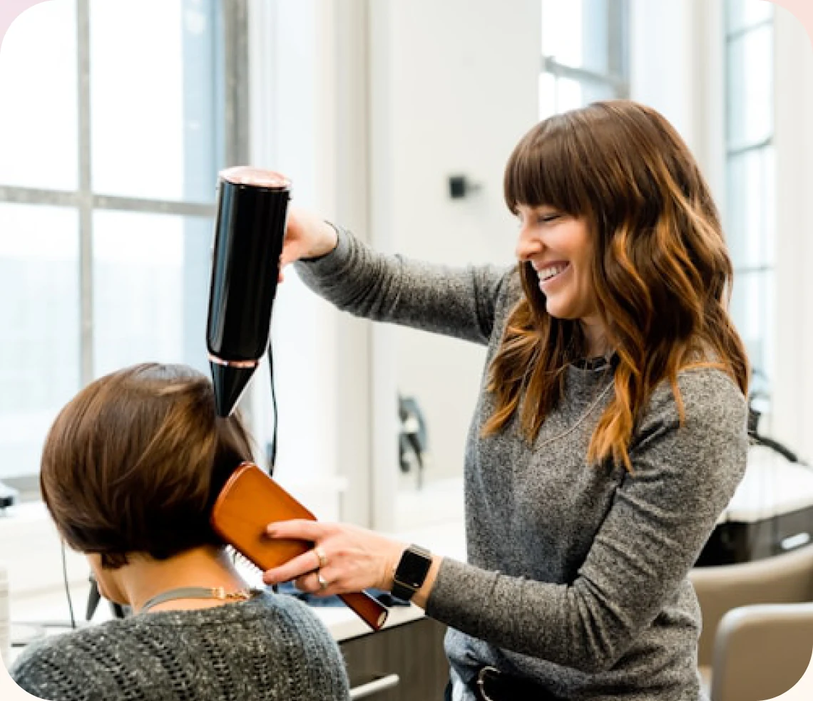 A stylist blow-drying a client’s hair in a beauty salon
