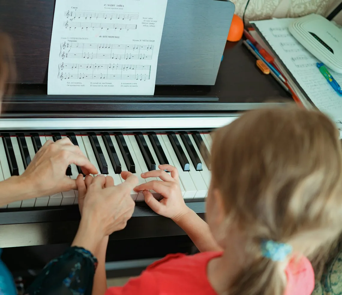 A teacher guiding a child’s hands at the piano