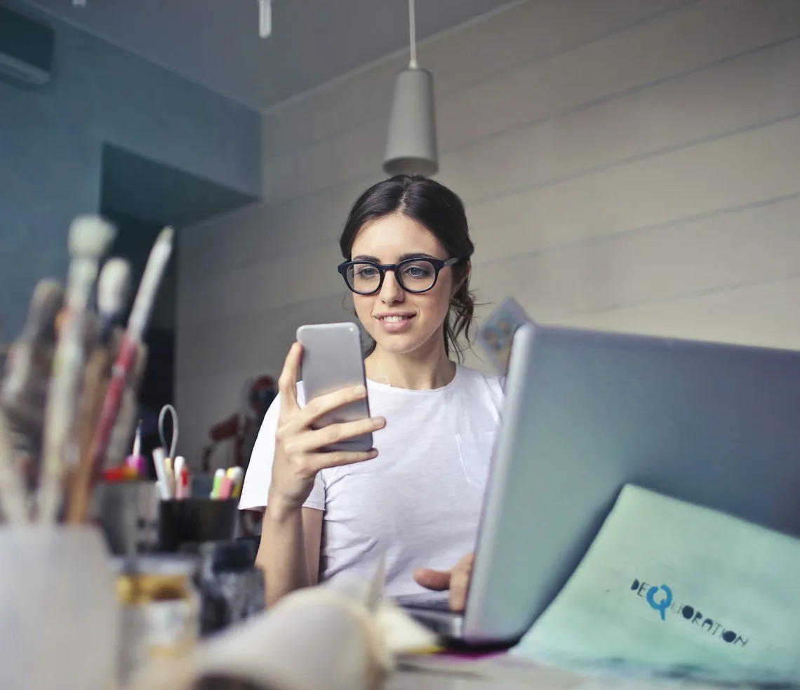 An SMM specialist planning posts with a phone and a laptop at the desk