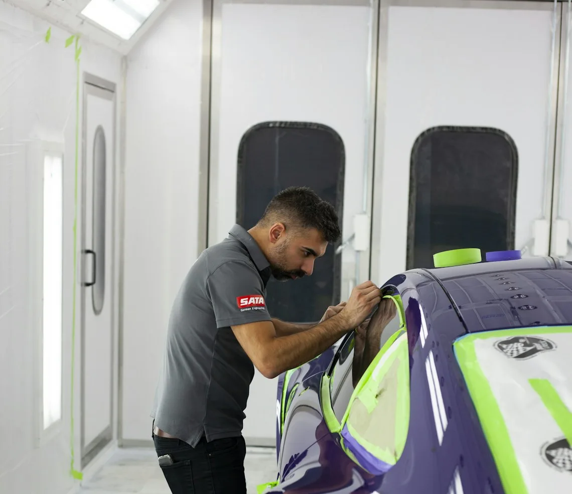 A technician masking a car before paint in the body shop bay